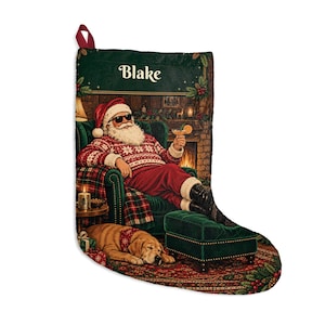 May include: A Christmas stocking featuring a printed scene of Santa Claus wearing sunglasses and a patterned sweater while sitting in a green armchair with a cocktail. The name Blake is printed at the top. A dog lies on a rug near a footstool.