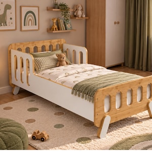 May include: A toddler bed featuring a natural wood frame with white side panels and safety rails. The bed includes a white mattress with a rainbow-patterned duvet, a green textured throw blanket, and a small brown teddy bear placed on the pillow.