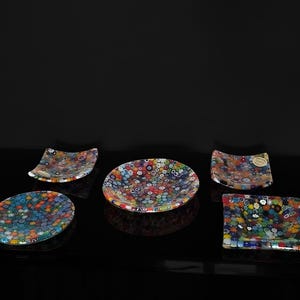 Può includere: Set di cinque piatti in vetro colorati con un motivo maculato. I piatti sono di varie forme e dimensioni, tra cui rotondi, quadrati e rettangolari.