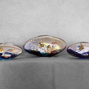 May include: Three glass paperweights shaped like pebbles, each containing a miniature underwater scene with colorful fish and coral. The paperweights are clear glass with a silver iridescent finish.