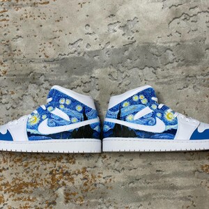 May include: Pair of white and blue high-top sneakers featuring a custom design inspired by Van Gogh's "Starry Night" painting. The design includes swirling blue skies, yellow stars, and a dark silhouette of a town.