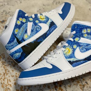 May include: Pair of white and blue high-top sneakers with a custom design inspired by Van Gogh's "Starry Night" painting. The design features swirling blue, yellow, and black brushstrokes. The sneakers have white laces and a white Nike swoosh.