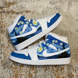 May include: Pair of white and blue sneakers with a custom design inspired by Van Gogh's "Starry Night" painting. The shoes feature a white swoosh, blue accents, and a starry night sky design on the sides.