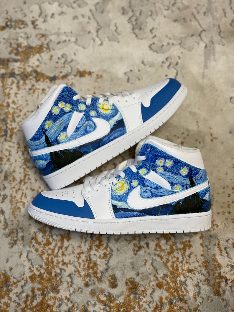 May include: Pair of white and blue sneakers with a custom design inspired by Van Gogh's "Starry Night" painting. The shoes feature a white swoosh, blue accents, and a starry night sky design on the sides.