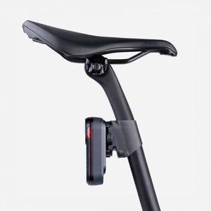 Könnte beinhalten: Ein schwarzer Fahrradsattel und eine Sattelstütze mit einem roten und grauen Rücklicht. Der Sattel ist gebogen und trägt den Aufdruck "PRIME". Das Rücklicht ist rechteckig und hat ein rotes Licht.