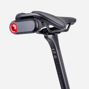 Op de afbeelding: Een zwart fietszadel gemonteerd op een zwarte zadelpen met een rood en zwart achterlicht aan de achterzijde. De zadelpen bevat witte tekstmarkeringen waaronder BMC, SP AS10, 10-385 en min. insertion 80 mm, samen met een verticale schaal.