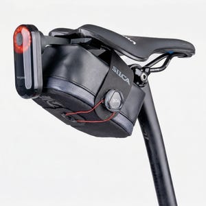 May include: A black bicycle saddle bag with a BOA closure system and the brand name SILCA printed on the side. The bag is mounted under a black bicycle seat and features a red LED tail light attached to the rear, with a visible Magene logo.