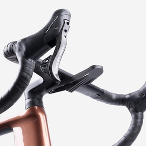 Puede incluir: Primer plano de un manillar de bicicleta con cinta negra y manetas de freno. El cuadro es de color bronce. Las manetas de freno tienen el texto "CAMPAGNOLO" y "SUPER RECORD" impreso.