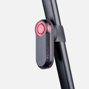 Könnte beinhalten: Ein schwarzes Garmin Fahrrad-Radar-Rücklicht mit einer kreisförmigen roten Linse an der Oberseite und einem vertikalen roten Lichtstreifen an der Seite. Das Gerät ist mit einem schwarzen Gummiband an einer schwarzen, zylindrischen Sattelstütze befestigt.