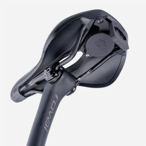 May include: A black bicycle saddle attached to a Roval seatpost. The underside of the saddle features a circular mount with a logo, metal rails, and a rear-facing bracket. The seatpost is marked with the Roval brand name in grey lettering.
