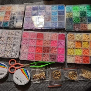 May include: A collection of jewelry-making supplies, including various colored beads in clear plastic organizers, spools of elastic string, scissors, tweezers, and small bags of gold-colored findings and hoop earrings. The beads are arranged by color, offering a wide range of options.