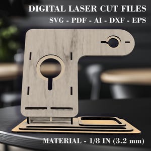 May include: Laser cut file design for a phone stand with a small tray. The stand is made of wood and has a light brown color. The design includes a phone holder, a small tray, and a slot for charging cables. The file is available in SVG, PDF, AI, DXF, and EPS formats. The material thickness is 1/8 inch (3.2 mm).