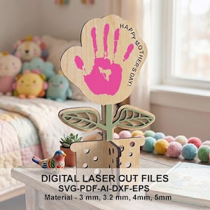 Puede incluir: Decoración de madera para el Día de la Madre con forma de flor, con una huella de mano rosa y el texto "Happy Mother's Day!". La flor está en una maceta de madera con hojas y un tallo. También se ve una pequeña figura de pájaro y una planta suculenta.