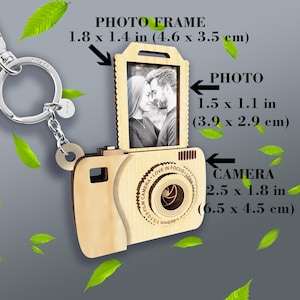 May include: Wooden camera keychain with a photo frame insert. The frame is 1.8 inches by 1.4 inches and the camera is 2.5 inches by 1.8 inches. The camera has a lens with the words "Camera, Love in Focus, Lens" engraved around it.