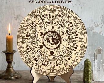 May include: A circular wooden 2027 lunar calendar featuring laser-cut text and graphics, including months, zodiac signs, moon phases, and a central tree design. The text reads DIGITAL LASER CUT FILES SVG-PDF-AI-DXF-EPS and 2 VERSIONS: NY TIME (EST/EDT) & UTC.