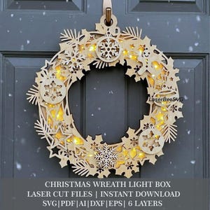 Può includere: Una ghirlanda luminosa circolare realizzata in legno chiaro a strati con ritagli di fiocchi di neve, stelle, un omino di pan di zenzero e ornamenti. Luci LED giallo caldo brillano dall'interno. Il testo LaserBeeSVG è visibile.