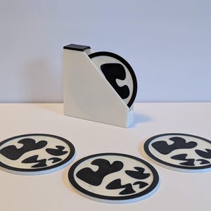 May include: Set of four black and white coasters with a unique abstract design. The coasters are in a white holder.