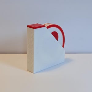 May include: A white coaster holder with a red accent on top, holding several red and white coasters. The coasters have a target design. The text "dekadebydekade" and "@dekadebydekade" is printed on the side of the holder.