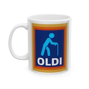 Puede incluir: Taza de cerámica blanca con un diseño azul, naranja y amarillo. El diseño presenta una figura de palo azul con un bastón y la palabra "OLDI" en letras blancas. La taza tiene un asa blanca.