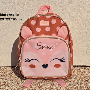 Op de afbeelding: Een bruine en roze rugzak met een vossengezicht en de naam Emma op het voorvak. De rugzak heeft kleine oortjes, een glinsterende gouden rand en meet 29 bij 23 bij 10 cm. De rugzak is voorzien van een stippenpatroon.