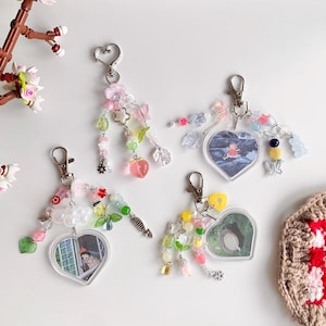 May include: Four heart-shaped keychains with colorful beads and charms. Each keychain features a different anime character in a clear plastic frame. The charms include butterflies, flowers, stars, and other small decorative elements.