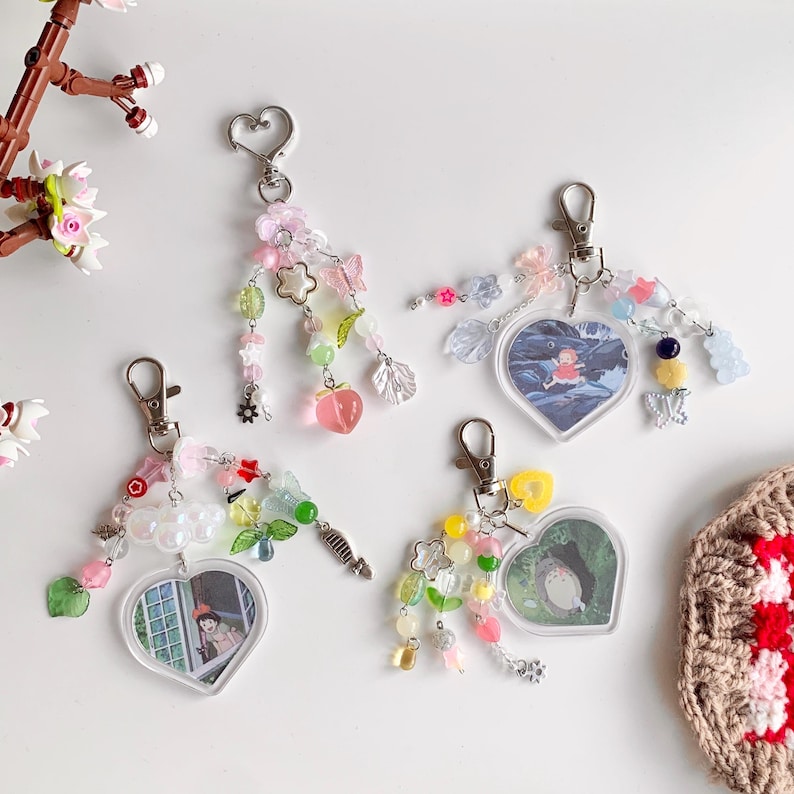 May include: Four heart-shaped keychains with colorful beads and charms. Each keychain features a different anime character in a clear plastic frame. The charms include butterflies, flowers, stars, and other small decorative elements.