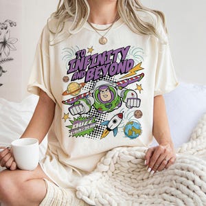 Puede incluir: Camiseta color crema con un dise&ntilde;o de Buzz Lightyear y el texto "To Infinity and Beyond". El dise&ntilde;o incluye planetas, un cohete y rayos. La camiseta tiene un corte holgado.