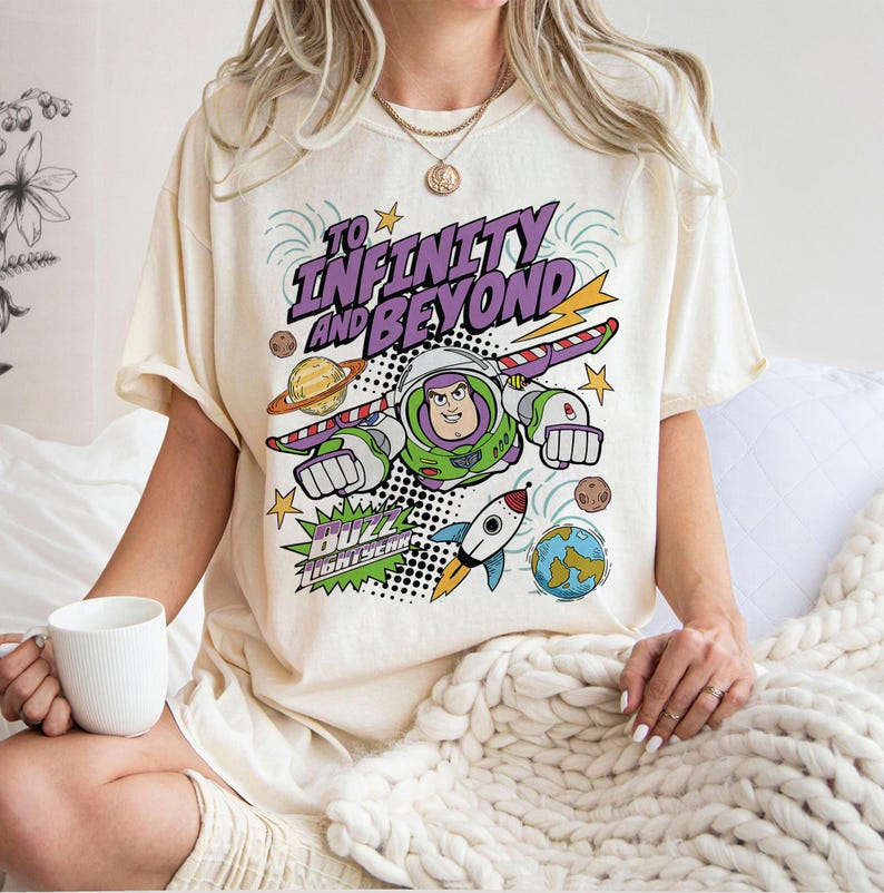 Puede incluir: Camiseta color crema con un dise&ntilde;o de Buzz Lightyear y el texto "To Infinity and Beyond". El dise&ntilde;o incluye planetas, un cohete y rayos. La camiseta tiene un corte holgado.