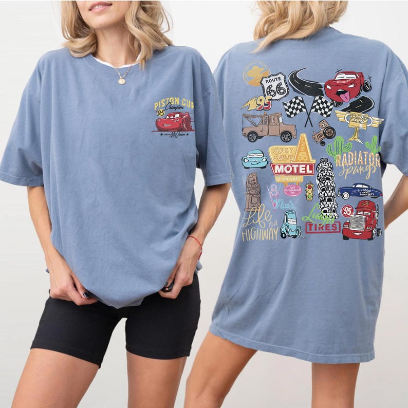 May include: Two light blue t-shirts featuring Cars movie graphics. One shirt has a small front graphic of Lightning McQueen with "Piston Cup 95". The other shirt has a large back graphic with various Cars characters and "Route 66" and "Radiator Springs" text.