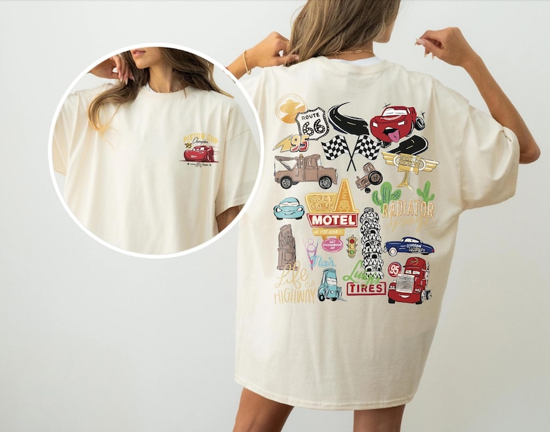 May include: Cream-colored t-shirt featuring a cartoon car design. The front has a small car graphic, while the back showcases a larger, colorful design with various car-themed illustrations, including Route 66 and checkered flags.