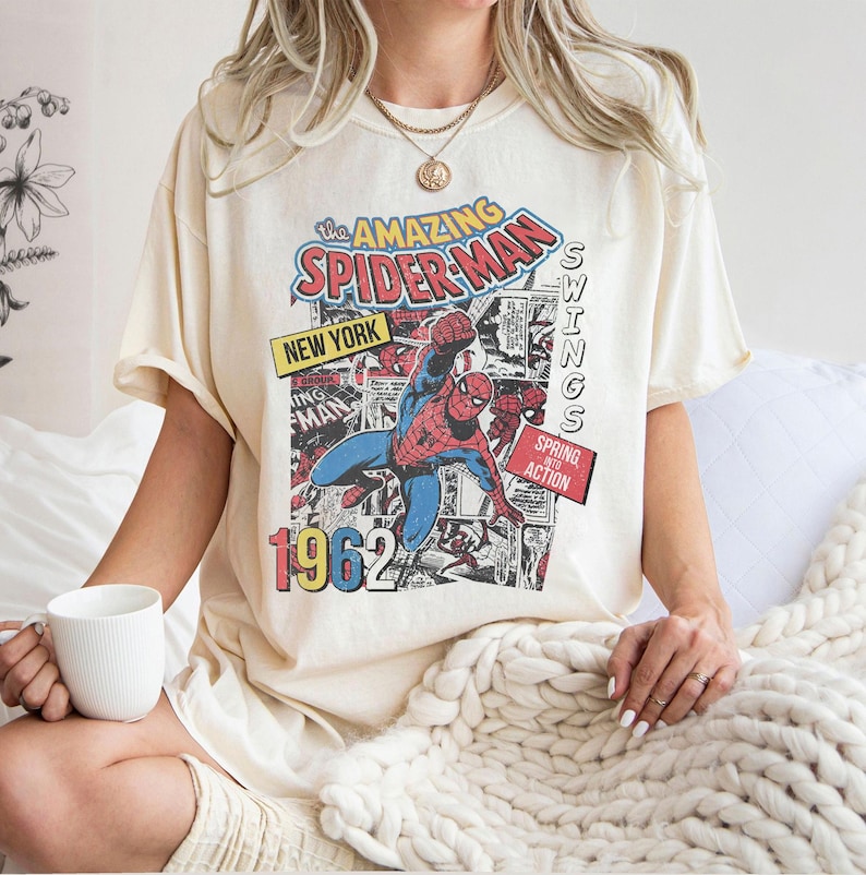 Peut inclure: T-shirt cr&egrave;me avec un graphisme de bande dessin&eacute;e vintage de Spider-Man. Le design comprend le texte "The Amazing Spider-Man", "New York" et "1962". Le super-h&eacute;ros est repr&eacute;sent&eacute; dans son costume rouge et bleu classique.