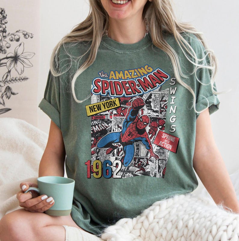 Peut inclure: T-shirt vert avec un design de couverture de bande dessin&eacute;e vintage de Spider-Man. Le graphisme comprend le texte "The Amazing Spider-Man", "New York" et "1962". Le super-h&eacute;ros est repr&eacute;sent&eacute; en action.