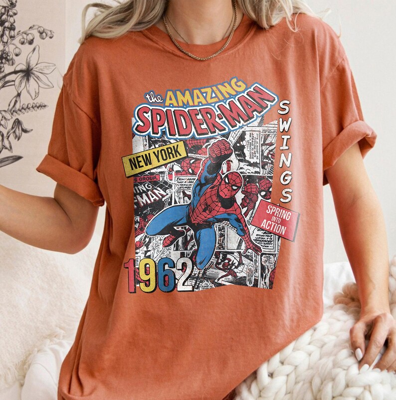 Peut inclure: T-shirt orange br&ucirc;l&eacute; avec un graphisme de bande dessin&eacute;e de Spider-Man. Le motif comprend le texte "The Amazing Spider-Man", "New York", "1962" et "Swings into Action". Le t-shirt a des manches courtes et une coupe d&eacute;contract&eacute;e.