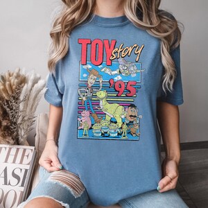 May include: Blue t-shirt featuring a graphic from the movie "Toy Story" with the text "Toy Story '95". The graphic includes images of Woody, Buzz Lightyear, Rex, Hamm, the Little Green Men, and Mr. Potato Head.
