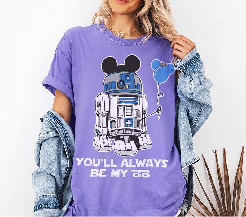 May include: A lilac-colored t-shirt featuring a mashup of R2-D2 and Mickey Mouse. The droid holds a blue balloon. The text "YOU'LL ALWAYS BE MY BB" is printed below the graphic. The shirt has short sleeves and a relaxed fit.