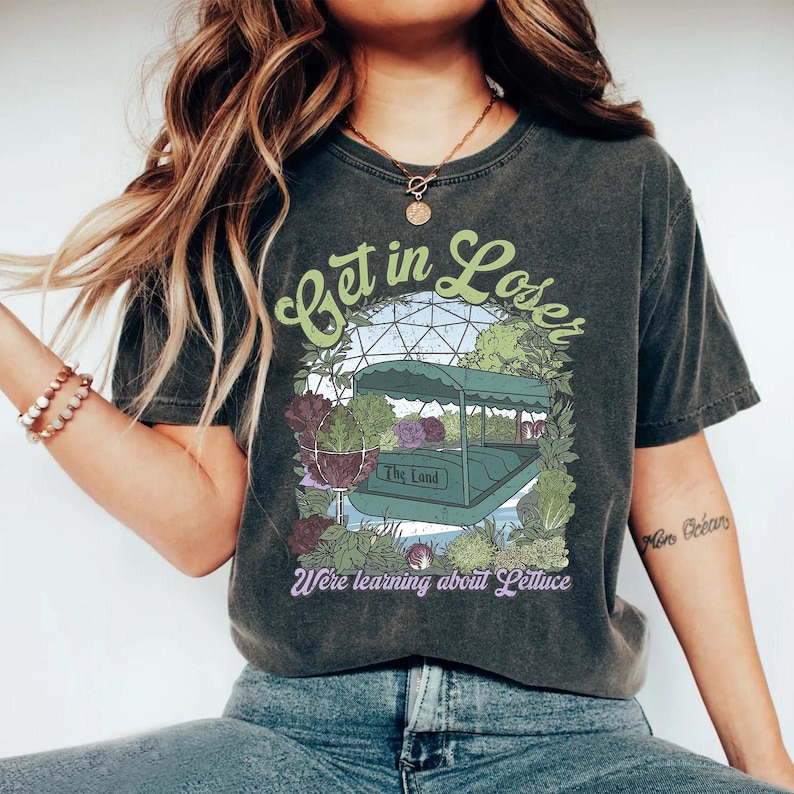 May include: Dark gray t-shirt with a graphic that says "Get in Loser" in green script. The graphic features a boat with plants and the text "The Land" and "We're learning about Lettuce".