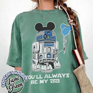 May include: Light green t-shirt featuring a graphic of R2-D2 with Mickey Mouse ears and a blue balloon. The text "YOU'LL ALWAYS BE MY BB" is printed below the graphic. The shirt has the words "Comfort Colors" and "Light Green" printed on it.