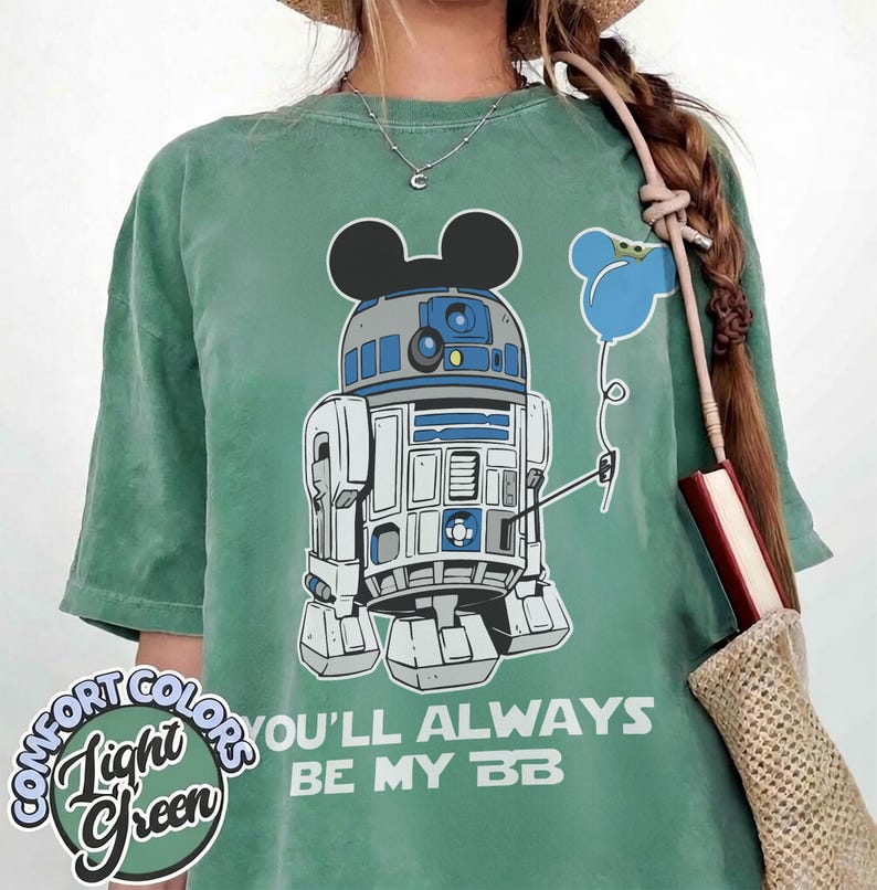 May include: Light green t-shirt featuring a graphic of R2-D2 with Mickey Mouse ears and a blue balloon. The text "YOU'LL ALWAYS BE MY BB" is printed below the graphic. The shirt has the words "Comfort Colors" and "Light Green" printed on it.
