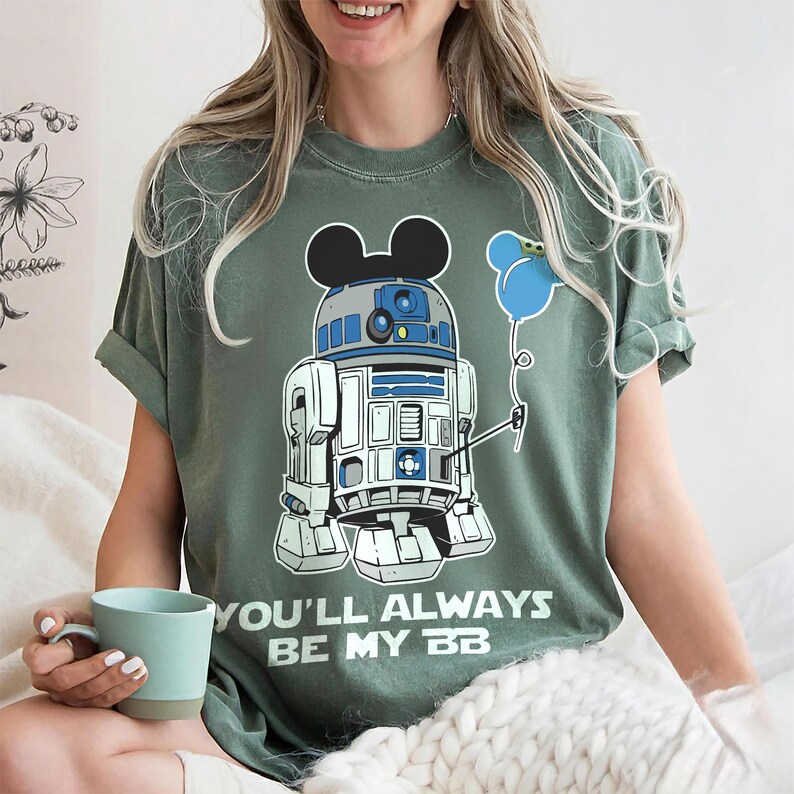 May include: Green t-shirt featuring a cartoon R2-D2 character with Mickey Mouse ears and a blue balloon. The text "YOU'LL ALWAYS BE MY BB" is printed below the graphic. The shirt is a relaxed fit.