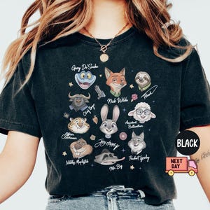 May include: A black short-sleeve t-shirt featuring a graphic print of various animated animal characters including Nick Wilde, Judy Hopps, and Flash. The design includes character names written in script and small star icons scattered across the front.