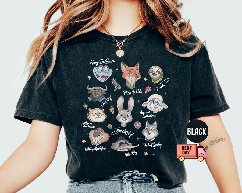 May include: A black short-sleeve t-shirt featuring a graphic print of various animated animal characters including Nick Wilde, Judy Hopps, and Flash. The design includes character names written in script and small star icons scattered across the front.