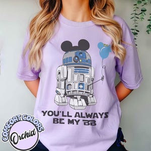 May include: A light purple Comfort Colors t-shirt featuring a graphic of R2-D2 with Mickey Mouse ears and a blue balloon. The text "YOU'LL ALWAYS BE MY BB" is printed below the graphic. A Comfort Colors Orchid logo is on the bottom left.
