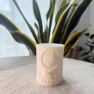 Puede incluir: Vela de pilar de color marfil con un dise&ntilde;o en relieve detallado. El dise&ntilde;o incluye una luna creciente, estrellas y elementos arquitect&oacute;nicos que se asemejan a mezquitas. La vela tiene una mecha central.