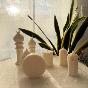Puede incluir: Una colecci&oacute;n de velas de color marfil en varias formas, incluyendo dise&ntilde;os cil&iacute;ndricos, en forma de c&uacute;pula y de pilar. Algunas velas presentan patrones intrincados y detalles arquitect&oacute;nicos, creando un ambiente c&aacute;lido y acogedor. Las velas est&aacute;n dispuestas sobre una superficie de tonos neutros.