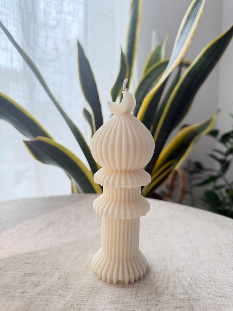 Puede incluir: Vela de color marfil con un dise&ntilde;o &uacute;nico. La vela presenta una estructura en capas con una luna creciente en la parte superior. La vela tiene una textura acanalada y mide aproximadamente 15 cm de altura. La vela no tiene perfume y es adecuada para la decoraci&oacute;n del hogar.