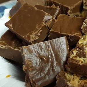Peut inclure: Gros plan sur une assiette remplie de morceaux de fudge au chocolat. Le fudge est d'une riche couleur brun foncé et semble fraîchement préparé. Certaines pièces ont un dessus lisse, d'autres une surface légèrement texturée. Le fudge est coupé en carrés irréguliers.