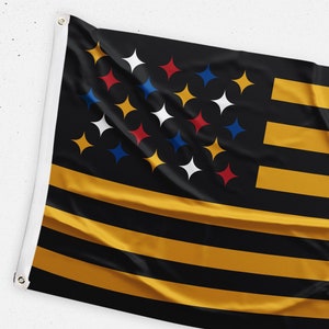 May include: A black and gold flag with a design of stars in red, white, blue, and yellow. The stars are arranged in a circle in the upper left corner of the flag.