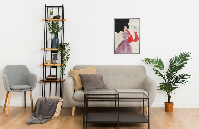 K&ouml;nnte beinhalten: Ein Wohnzimmer-Interieur mit einem grauen Sofa, zwei schwarzen Glas-Couchtischen, einem grauen Sessel, einem schwarzen Metall-Leiterregal mit Holzb&ouml;den, einer Topfpalme und einem gerahmten Druck einer Frau in einem roten Kleid mit dem Text "Knowing the wild one".