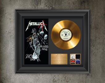 May include: A framed Metallica And Justice For All gold record display featuring a black frame, a gold vinyl disc, the album cover art with signatures, a descriptive plaque, and a small collage of four album covers on a dark background.