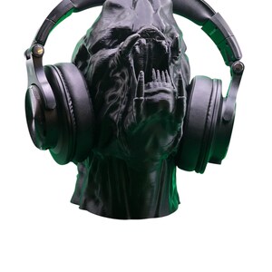Op de afbeelding: Een zwart 3D-geprint beeld van een schepsel met een wijd open mond, met een zwarte over-ear koptelefoon.